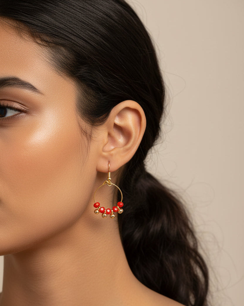 Gold hoop earrings with red beads on a white background