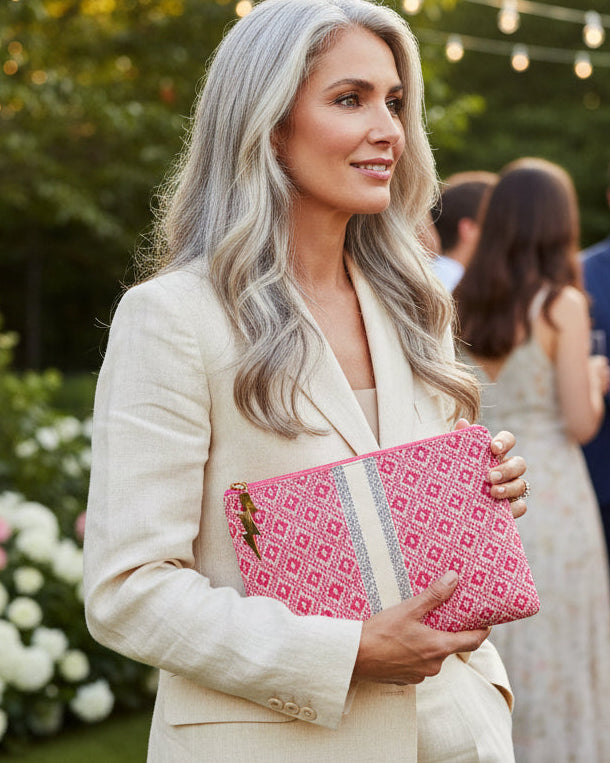 Woman holding a pink clutch with a patterned strap outdoors