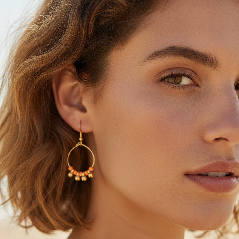 Gold hoop earrings with orange beads on a white background