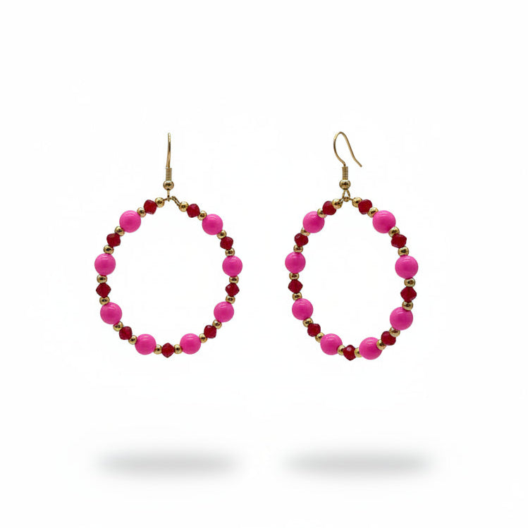 Pink and dark red beaded hoop earrings with gold hooks, displayed on a black metal stand against a light gray background.